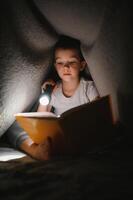 Portrait of cute little boy reading in bed with flashlight in dark room, enjoying fairytales photo