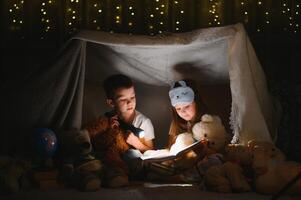 contento familia niños leyendo un libro con un Linterna en un tienda a hogar foto