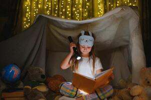 un bonito pequeño niña leyendo un libro en el piso debajo el lámpara. niños y educación. foto