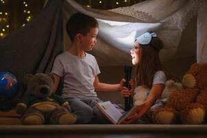 children boy and girl playing and frighten each other with flashlight in tent at night photo