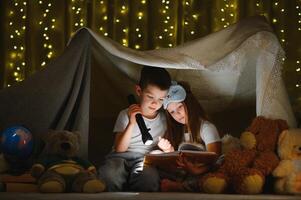 contento familia niños leyendo un libro con un Linterna en un tienda a hogar foto