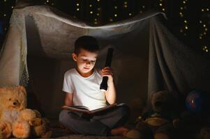 Preteen boy with flashlight reading book at home photo
