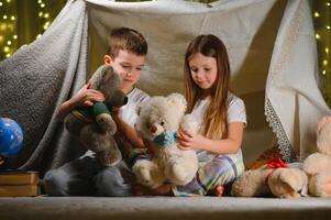 kids lying on floor in cozy nursery. Boy and girl holding flashlights in hands. Children play in a makeshift tent in the nursery. photo