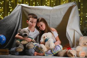 Two little child play at home in the evening to build a camping tent to read books with a flashlight and sleep inside. photo