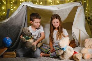 Two little child play at home in the evening to build a camping tent to read books with a flashlight and sleep inside. photo