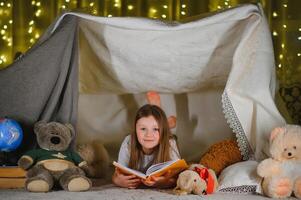 happy child girl laughing and reading book in dark in a tent at home photo