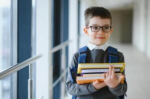 colegial con bolsa para la escuela y libros en el escuela. educación concepto. espalda a escuela. colegial yendo a clase. elegante chico con mochila. chico Listo a estudiar. foto