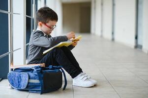 Happy cute clever boy in glasses with school bag and book in his hand. First time to school. Back to school photo