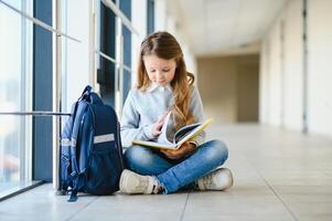 Front view of pretty blonde school girl holding many colorful notes and books. Clever teen girl smiling at camera, standing on corridor of international school. photo