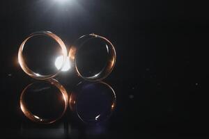 Elegant wedding rings for the bride and groom on a black background with highlights, macro, selective focus. photo