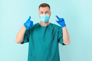 Vaccination against coronavirus. Testing COVID-19 vaccines. A male doctor in a medical mask fills a syringe the with a COVID-19 vaccine on a blue background. Doctor's hands hold a syringe close-up photo