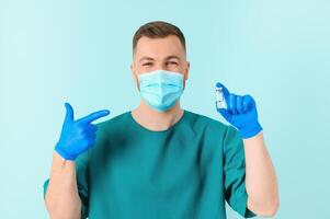 Vaccination against coronavirus. Testing COVID-19 vaccines. A male doctor in a medical mask fills a syringe the with a COVID-19 vaccine on a blue background. Doctor's hands hold a syringe close-up photo