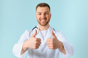 Waist up portrait view of the smiling happy doctor showing big finger at the free space on blue background. Doctor and medicine concept. photo