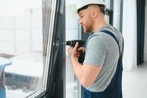 Workman in overalls installing or adjusting plastic windows in the living room at home photo