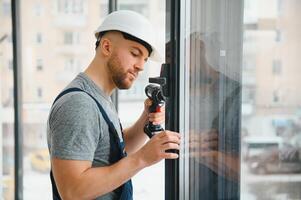 Construction worker using drill while installing window indoors photo