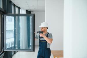 Construction worker repairing plastic window with screwdriver indoors, space for text. Banner design photo