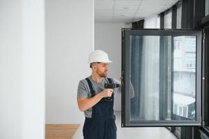 Workman in overalls installing or adjusting plastic windows in the living room at home photo