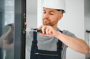 Workman in overalls installing or adjusting plastic windows in the living room at home photo