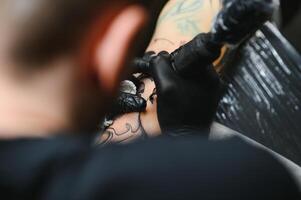 recortado cerca arriba de un barbado tatuaje artista trabajando a su estudio tatuajes manga en el brazo de su masculino cliente. hombre consiguiendo tatuado por profesional tatuador foto