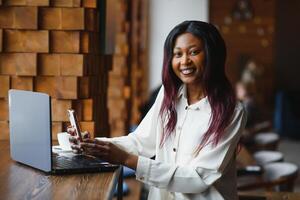 Happy african american woman worker using laptop work study at computer in loft office or cafe, smiling mixed race female student freelancer using pc app dating communicating online watching webinar photo