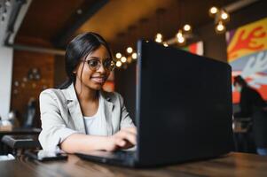 Young African American girl sitting in restaurant and typing on her laptop. Pretty girl working on computer at cafe. photo