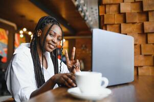 Head shot portrait of happy smiling African American woman sitting at table in cafe, looking at camera, excited female posing, working at computer, doing homework, preparing report in coffee house photo