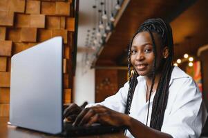 Head shot portrait of happy smiling African American woman sitting at table in cafe, looking at camera, excited female posing, working at computer, doing homework, preparing report in coffee house photo