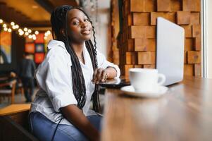 Head shot portrait of happy smiling African American woman sitting at table in cafe, looking at camera, excited female posing, working at computer, doing homework, preparing report in coffee house photo