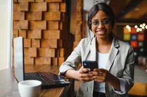 Head shot portrait of happy smiling African American woman sitting at table in cafe, looking at camera, excited female posing, working at computer, doing homework, preparing report in coffee house photo