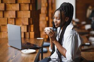 Young African American girl sitting in restaurant and typing on her laptop. Pretty girl working on computer at cafe. photo