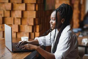 portrait of a smiling young african american woman sitting at cafe with laptop photo