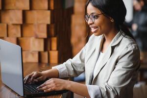 Happy african american woman worker using laptop work study at computer in loft office or cafe, smiling mixed race female student freelancer using pc app dating communicating online watching webinar photo