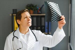 pretty female middle aged medical worker with x-ray standing by window photo