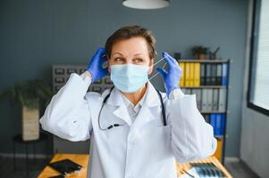 Portrait of a female doctor wearing face mask and holding her patient chart on digital tablet while standing at the hospital. photo