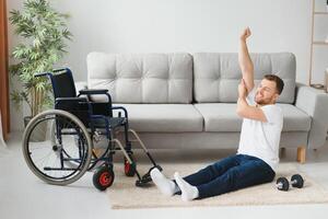 Man Disabled. Sports for Disabled. Male in Wheelchair with Dumbbells in Hands. Man with Dumbbells in Hands. Father Disabled Do Spotting. Sport at Apartment. Health Concept. Healthy Lifestyle photo