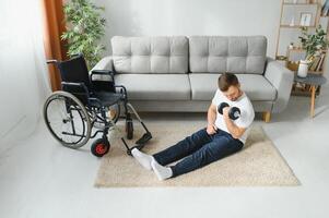 Man Disabled. Sports for Disabled. Male in Wheelchair with Dumbbells in Hands. Man with Dumbbells in Hands. Father Disabled Do Spotting. Sport at Apartment. Health Concept. Healthy Lifestyle photo