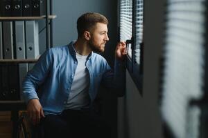 joven discapacitado hombre sentado en un silla de ruedas cerca el ventana foto