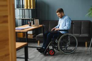 Handicapped Businessman Sitting On Wheelchair And Using Computer In Office photo