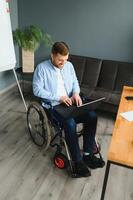 Disabled Businessman Sitting In Wheelchair Using Computer At Workplace photo