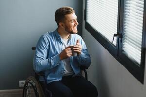 Young man in wheelchair near window indoors. Space for text photo