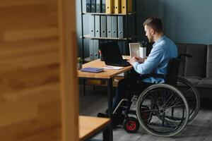 Handicapped Businessman Sitting On Wheelchair And Using Computer In Office. photo