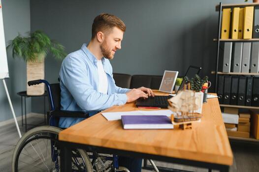 discapacitado persona en el silla de ruedas trabajos en el oficina a el computadora. él es sonriente y apasionado acerca de el flujo de trabajo. foto
