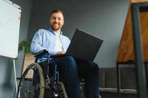 Disabled person in the wheelchair works in the office at the computer. He is smiling and passionate about the workflow. photo