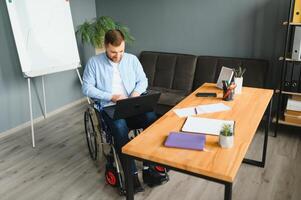 Disabled person in the wheelchair works in the office at the computer. He is smiling and passionate about the workflow. photo