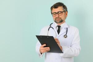 Senior doctor man wearing stethoscope and medical coat over blue background. Cheerful expression photo