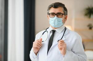 Mature old medical healthcare professional doctor wearing white coat, stethoscope, glasses and face mask. Medical staff health care protection concept. Portrait. photo
