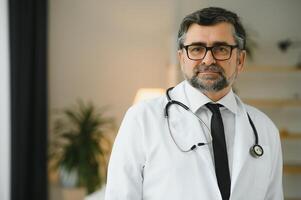 Portrait of healthcare worker. Image of senior male doctor wearing lab coat and standing at private clinic photo
