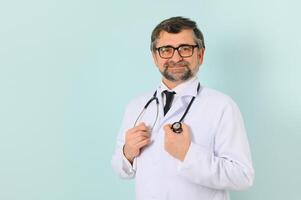 Senior doctor man wearing stethoscope and medical coat oveer blue background photo