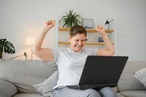 Excited mature woman looking at laptop screen, reading good news in message, celebrating online lottery win, rejoicing success, overjoyed older female sitting on couch at home, using computer. photo