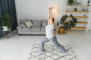 de edad mediana mujer haciendo yoga a hogar para extensión y siendo saludable. foto